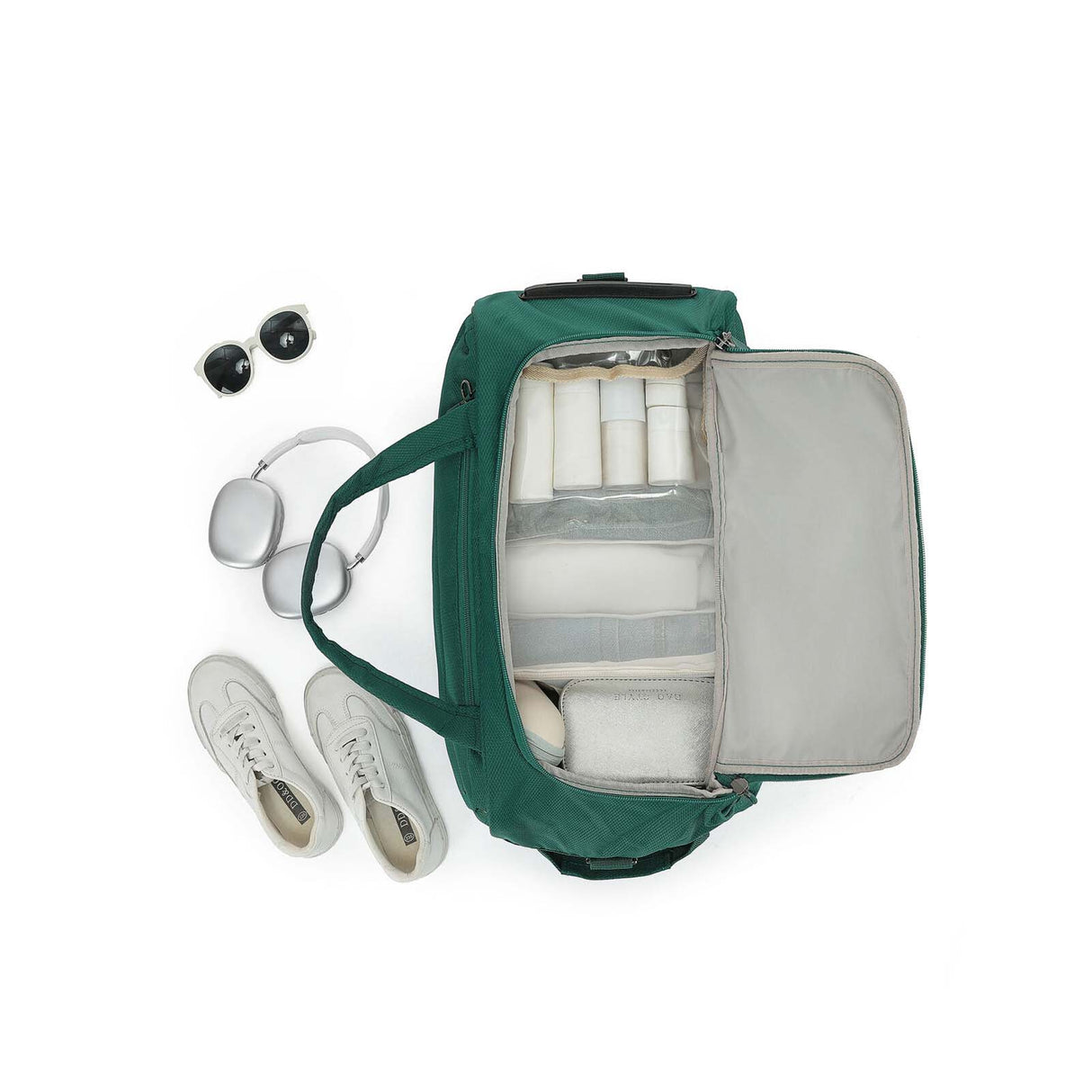 An Emerald Green Carry-On bag shown from above with its interior open, filled with travel items including white toiletry bottles, a gray organizer insert, and a small cooler. White sneakers, silver headphones, and black sunglasses are placed beside it on a clean white background.