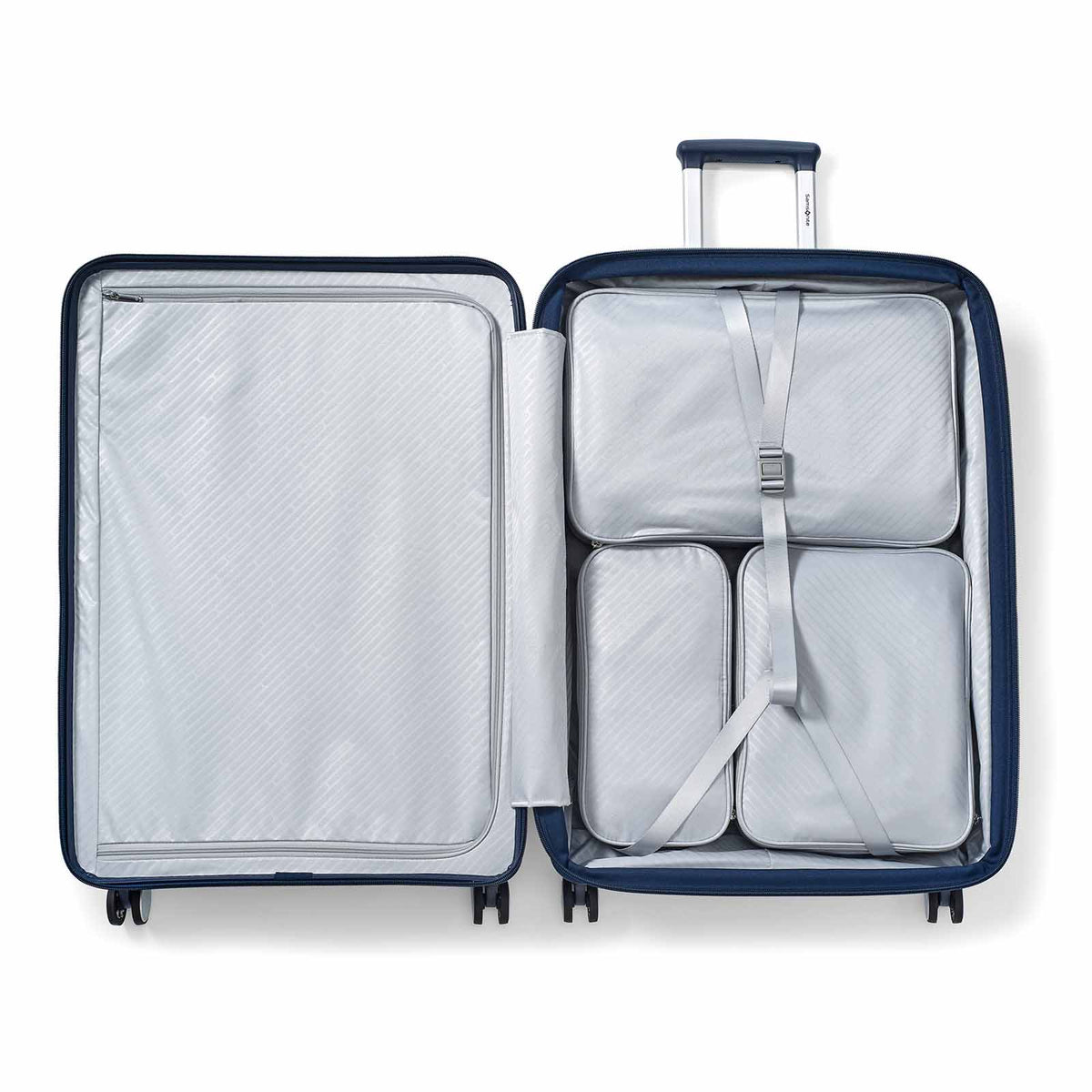 An open navy blue hard-shell suitcase shown from above, revealing a light gray interior with three packed travel organizers inside a mesh compartment and a telescoping handle extended.