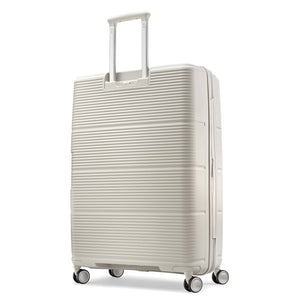 A cream-colored hardshell spinner suitcase with a textured horizontal ribbed pattern, featuring an extended telescoping handle and four multi-directional wheels, shown on a plain white background.