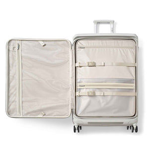 A hard-shell suitcase shown open from above, revealing a light beige interior with multiple zip compartments and elastic straps. The exterior shell is a pale metallic silver-gray, and the handle and wheels are visible against a clean white background.