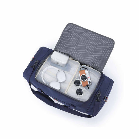 An open navy blue duffel bag with a transparent zippered compartment, shown on a white background. Inside, a gray geometric-patterned lid.