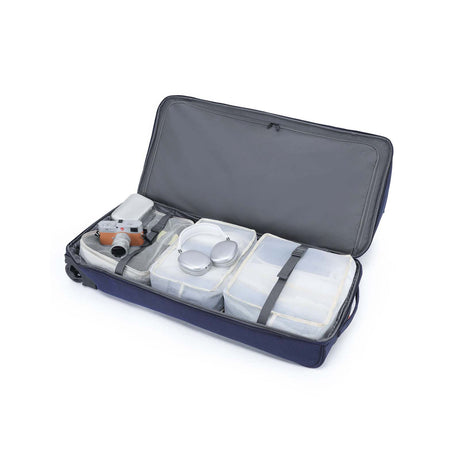 An open navy blue camera gear bag with gray interior lining, shown on a white background. Inside are several translucent plastic storage containers and straps, with a small camera accessory visible on the left side.